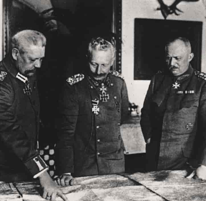 Sort-hvitt fotografi av Paul von Hindenburg, keiser Vilhelm 2 og Erich Ludendorff. De tre mennene er kledd i militære uniformer og ser ned på et kart som ligger på et bord foran dem.