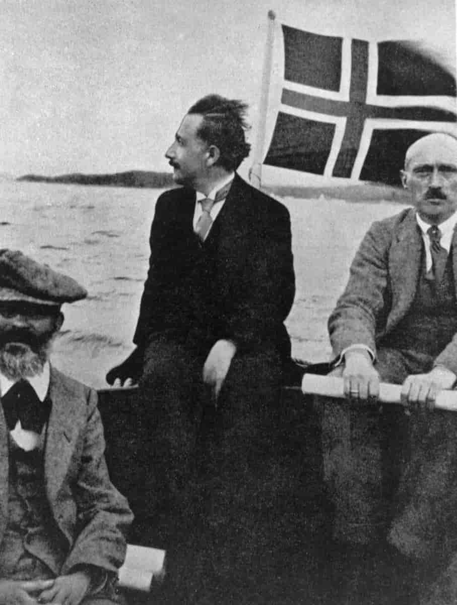 Svart-hvitt foto av tre menn i en båt med norsk flagg