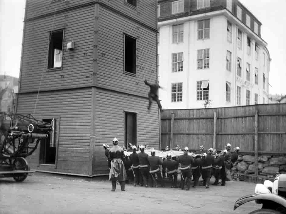 Hoppeseil demonstrert under en øvelse med hopp fra øvelsestårnet ved i Lars Hillesgate, Bergen i 1924-25. Til sammen er er det 22 brannmenn som holder seilet