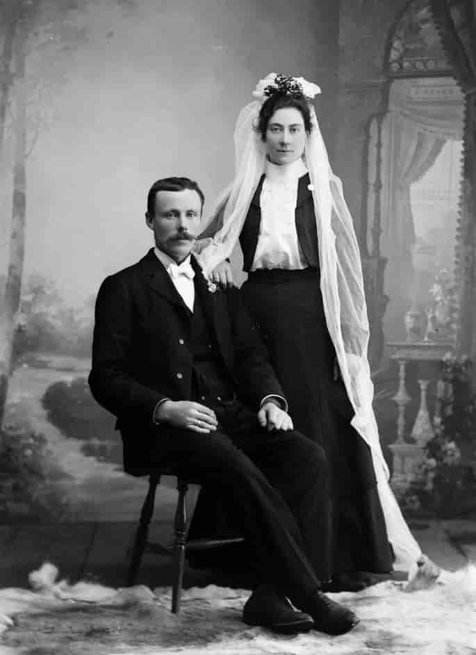 Et brudepar fotografert i et atelier omkring 1900. Bruden har langt slør.
