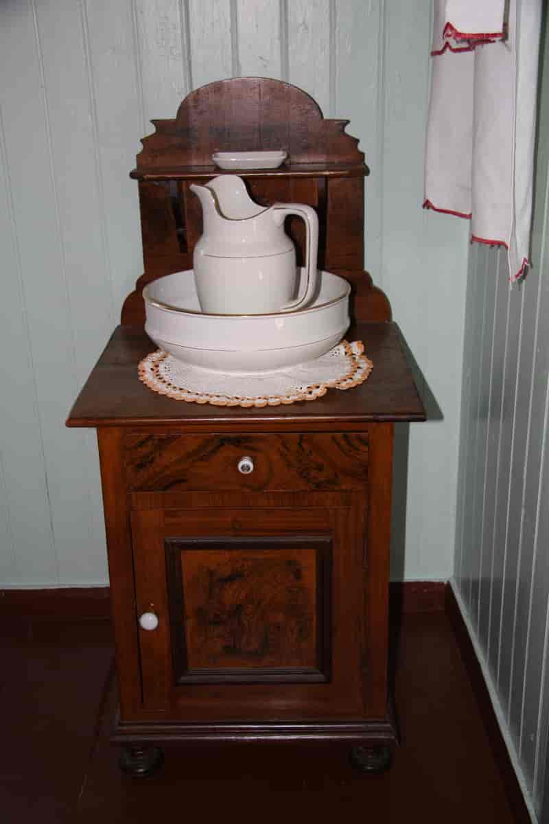 Vaskestell med mugge, vaskefat og såpekopp, plassert på en ådret servant fra ca. 1900.