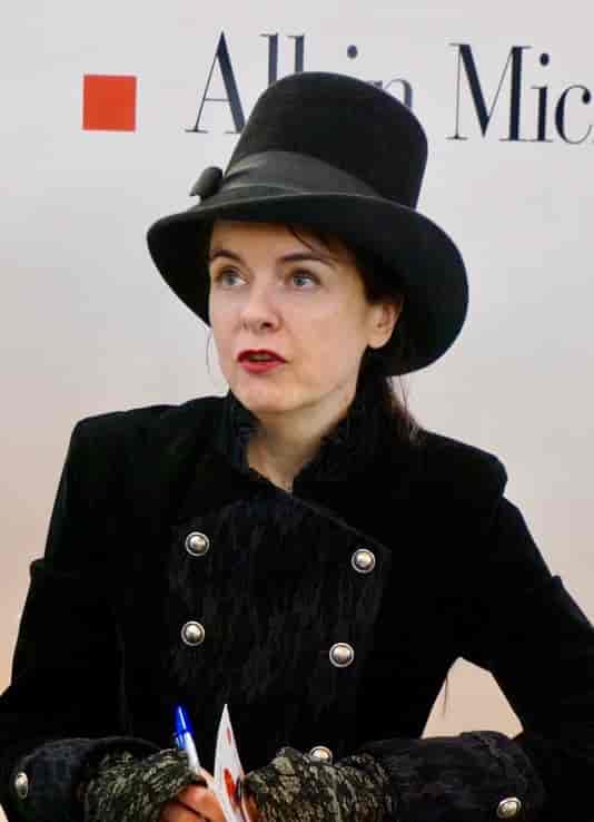 Amélie Nothomb i sort dobbetlspent jakke og høy sort hatt med sort bånd. 2015