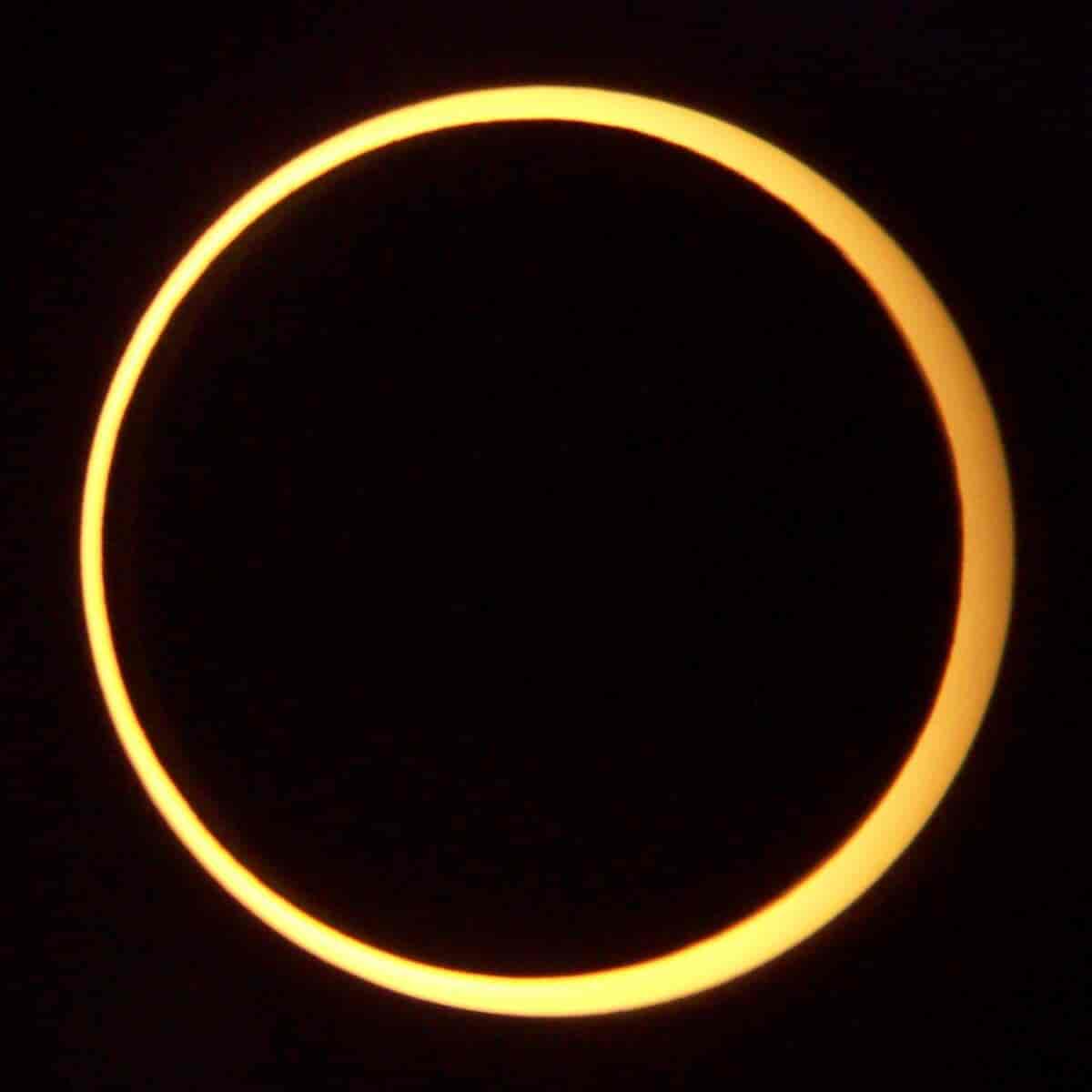 Svart himmel med en sort måne på. Den sorte månen er omgitt av en gullfarget ring som er sola. 