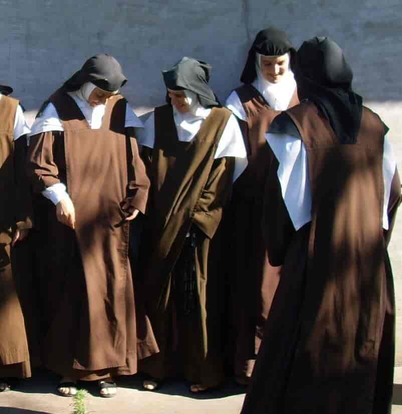 Fire nonner i lange, brune, enkle drakter. De har dekket til håret og skuldrene med hvitt tøy, og hodet er dekket av et svart hodetørkle