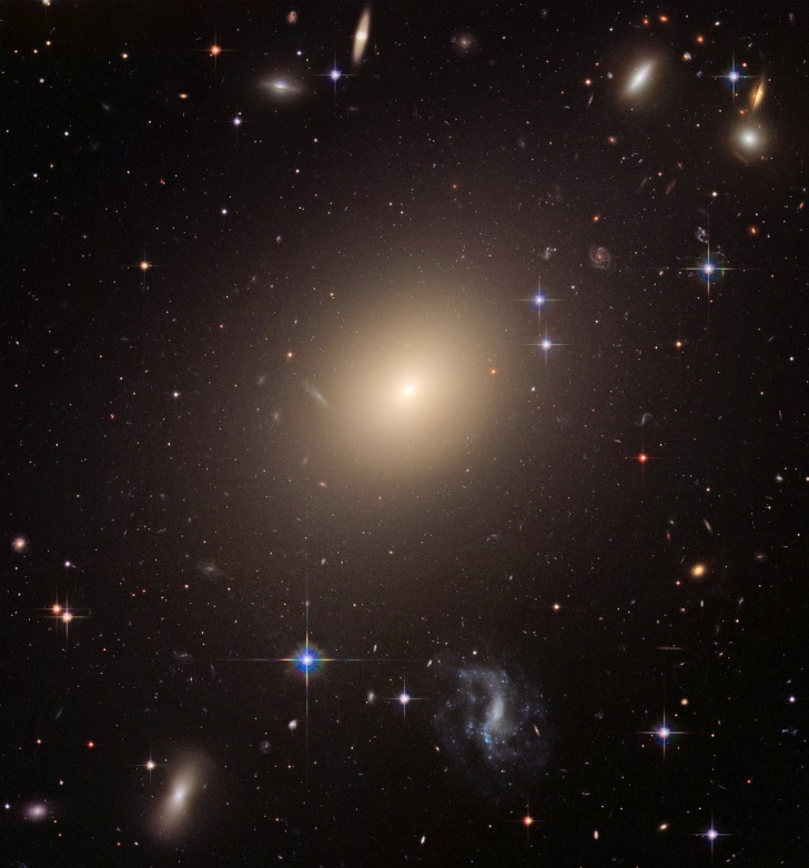 Bildet viser en galakse som består av mange små og store lysende prikker og noen støvskyer. Noen er blå, noen gule, noen hvite, noen rødaktige. Den viser svært forskjellige himmellegemer.