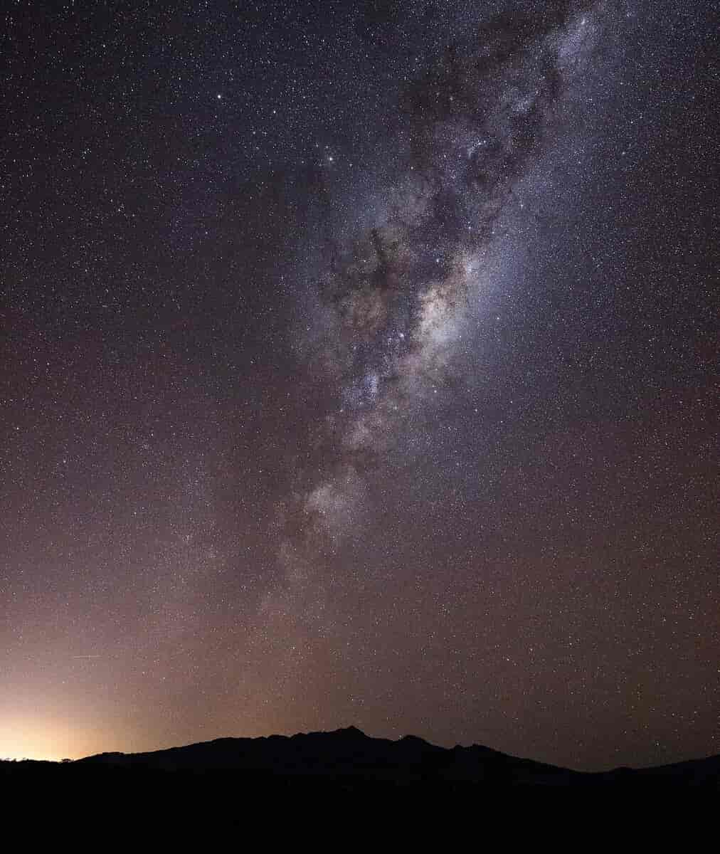 En mørk lilla nattehimmelen sett fra Jorda. Det lyser litt opp fra Jorda til venstre. Melkeveien ses som en slags sky av støv med små prikker som går opp fra noen svarte fjell og opp mot en lilla himmel.