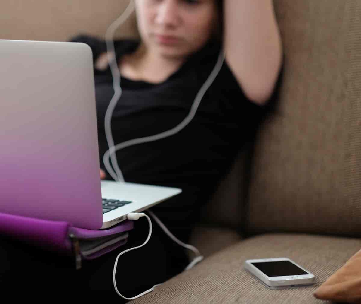 Ung jente som sitter med en mobiltelefon, datamaskin og øreplugger.