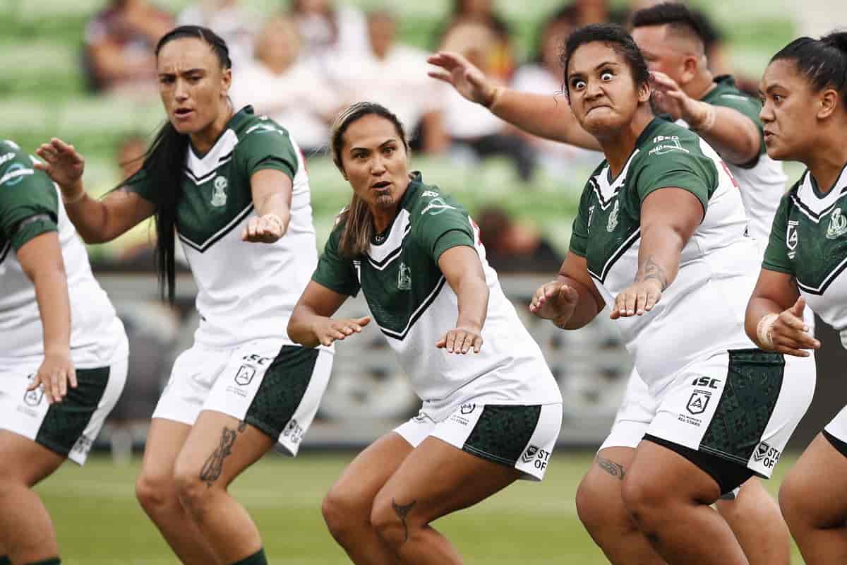 Fem kvinner i hvite og mørkegrønne rugbydrakter står på en rekke og bøyer knærne. De strekker armene framover og har har alvorlige, intense uttrykk i ansiktene. Foto