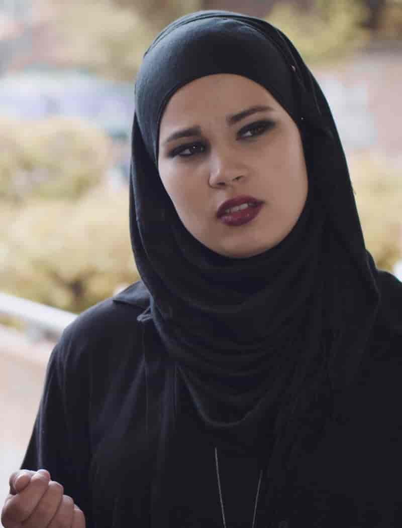 Fotografi av en kvinne med svart hijab og svarte klær. Hijaben er et skaut som dekker håret, ørene og halsen til kvinnen. 