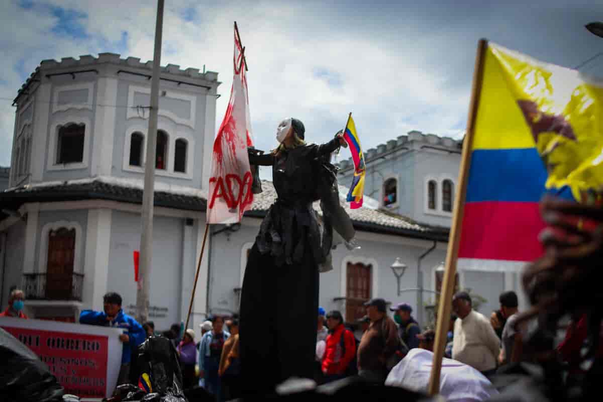 Fot av en folkemengde. En person står på stylter eller noe annet som gjør at hen er dobbelt så høy som resten. Noen holder plakater, noen har flagg fra Ecuaor.