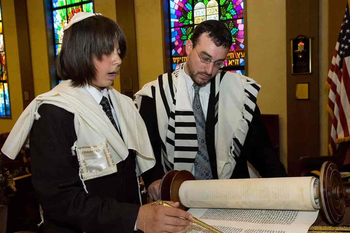 En jødisk gutt leser sammen med en voksen. Begge har kipa på hodet og et hvitt skjerf over skuldrene.