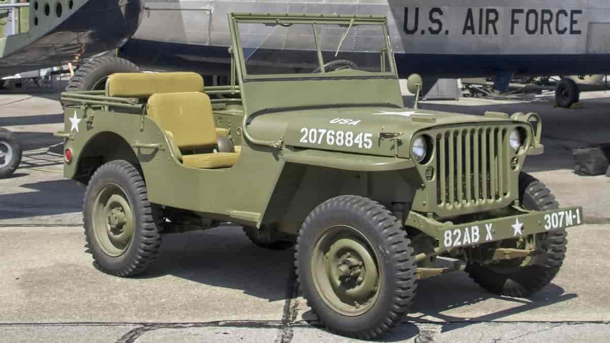 En militærgrønn bil av typen Jeep. I bakgrunnen et fly med skriften U. S. AIR FORCE. Foto