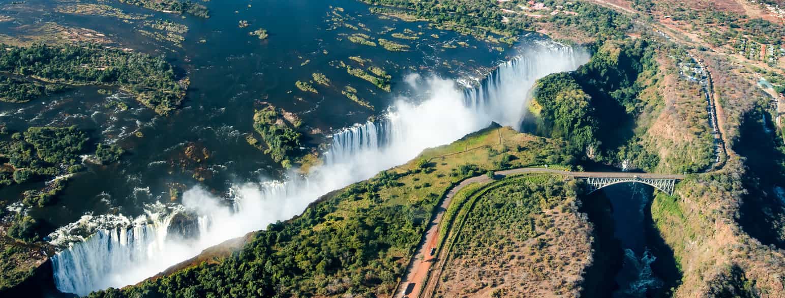 Victoriafallene er et av verdens høysete fossefall. Bildet er tatt fra Zambia. Broen går over til nabolandet Zimbabwe