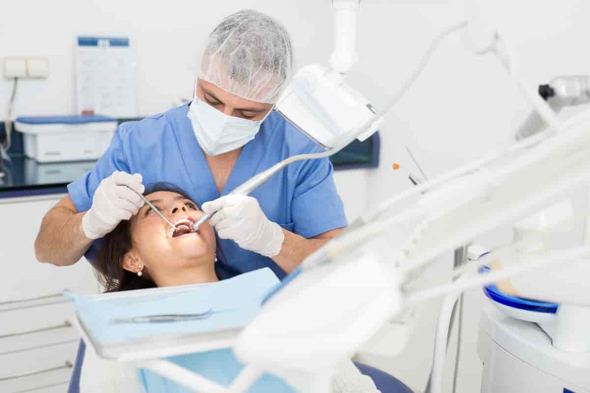 Tannlege ser inn i munnen på pasient. Ein kan sjå ei spesiell lampe på ein svingarm og eit svingbart bord med instrument på. 