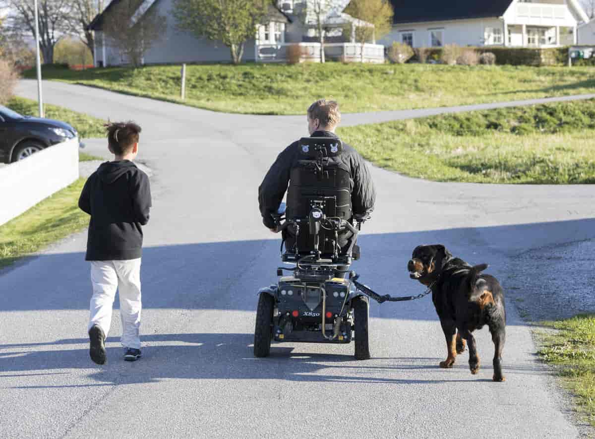 Foto av mann i rullestol som er på tur med sønnen og hunden sin