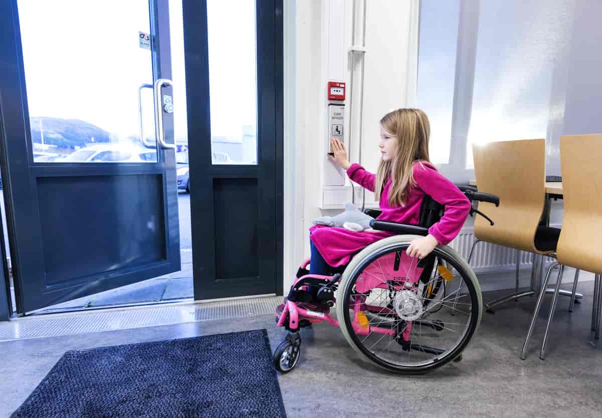 Jente i rullestol åpner dør med knapp
