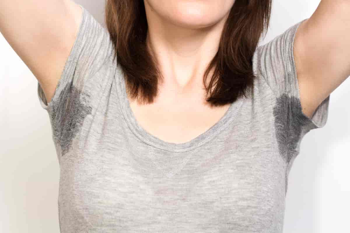 Kvinne i t-skjorte med våte flekker under begge armene. 