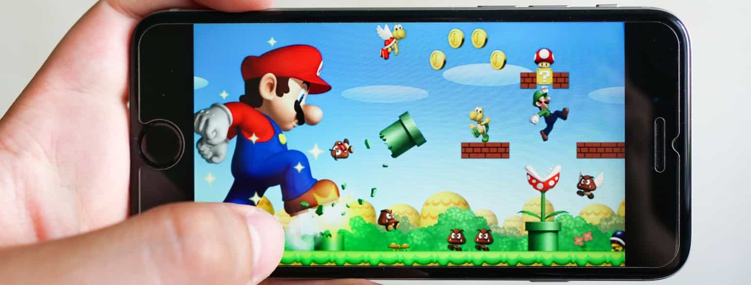 En hånd holder en iPhone med mobilspillet Super Mario Run på skjermen
