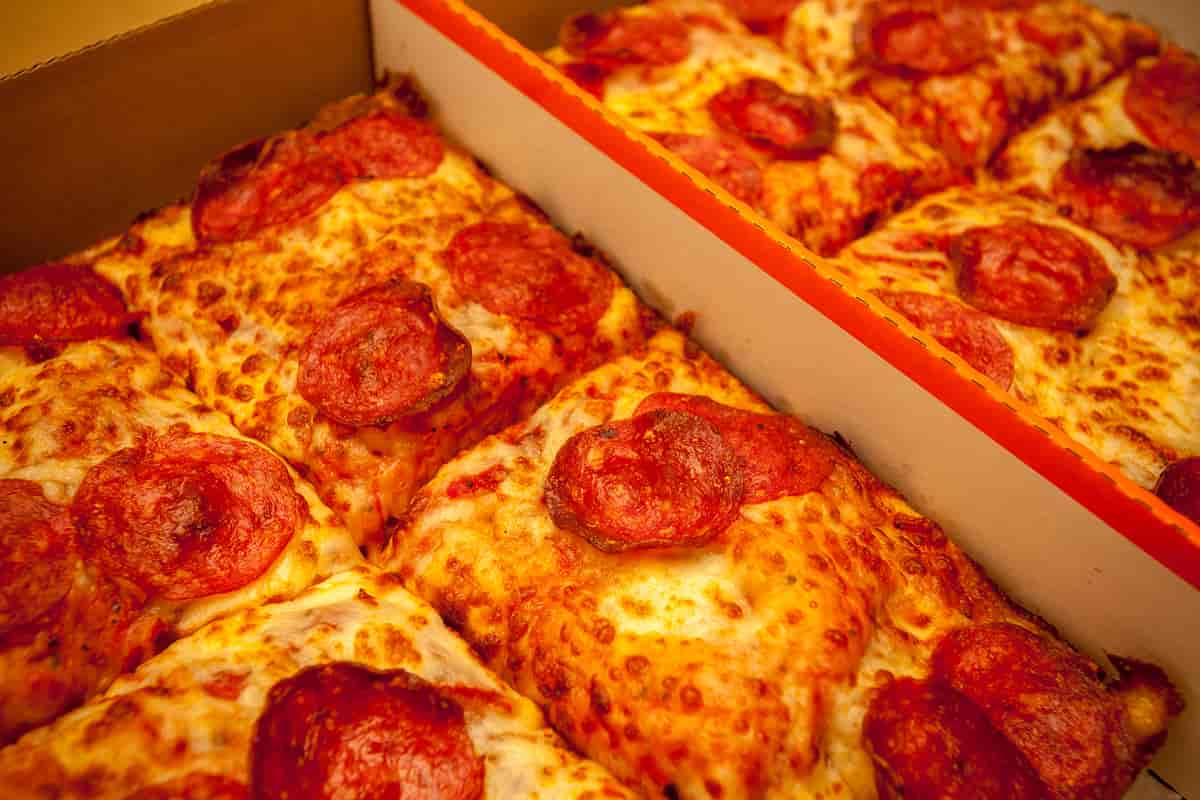 Pizza med ost og pepperoni kuttet i firkanta stykker ligger i en pizza-eske.
