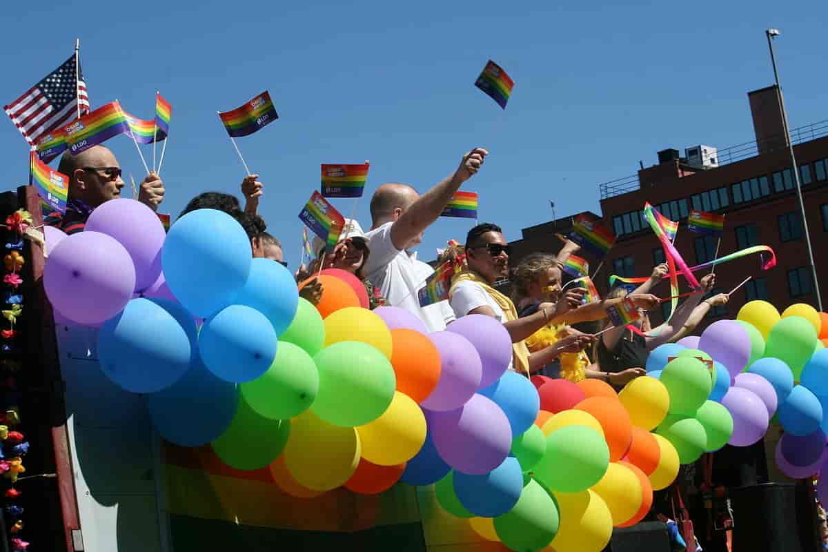 Menneske i ein parade med flagg og ballongar med i regnbogens fargar. Regnbogen er eit symbol for skeiv stoltheit. 