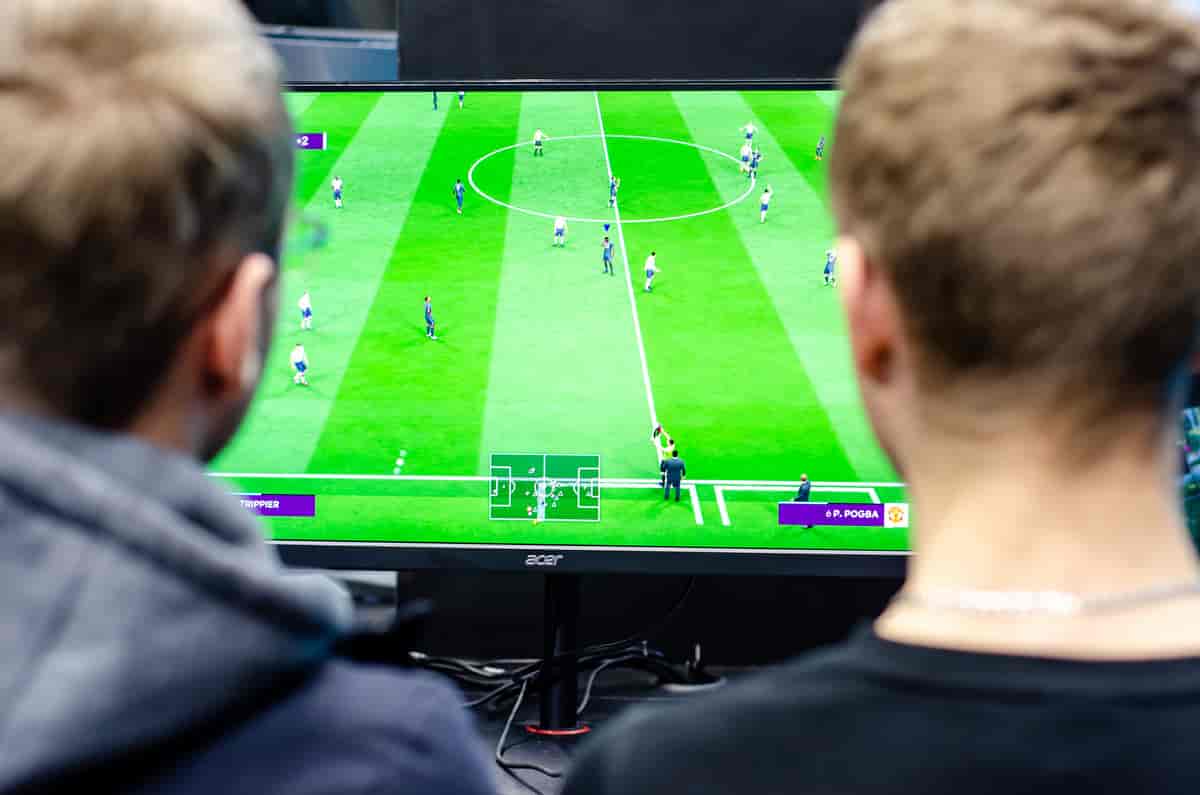 Foto av en TV-skjerm med et fotballspill og bakhodet til to gutter som sitter og spiller.