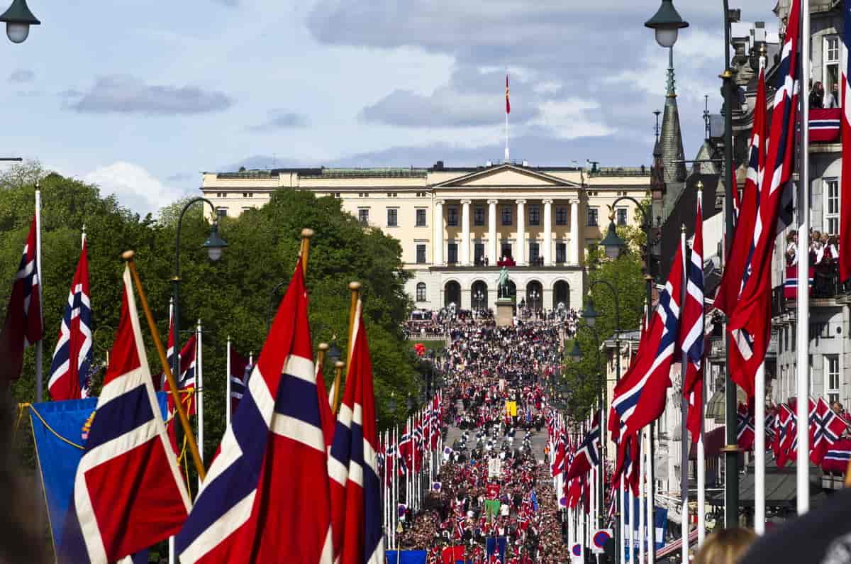 I forgrunnen er det mange flaggstenger med norske flagg. I enden av Karl Johan ligger slottet i bakgrunnen.