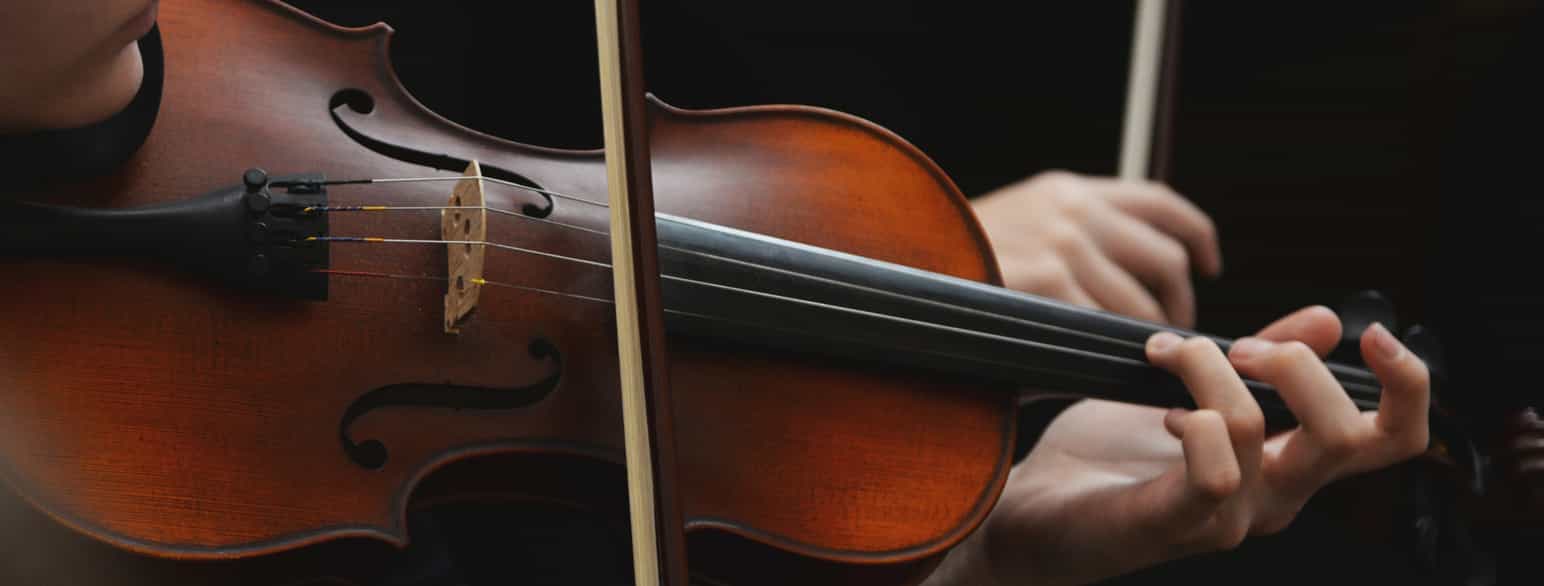 Nærbilde av en fiolin med bue og fingre.