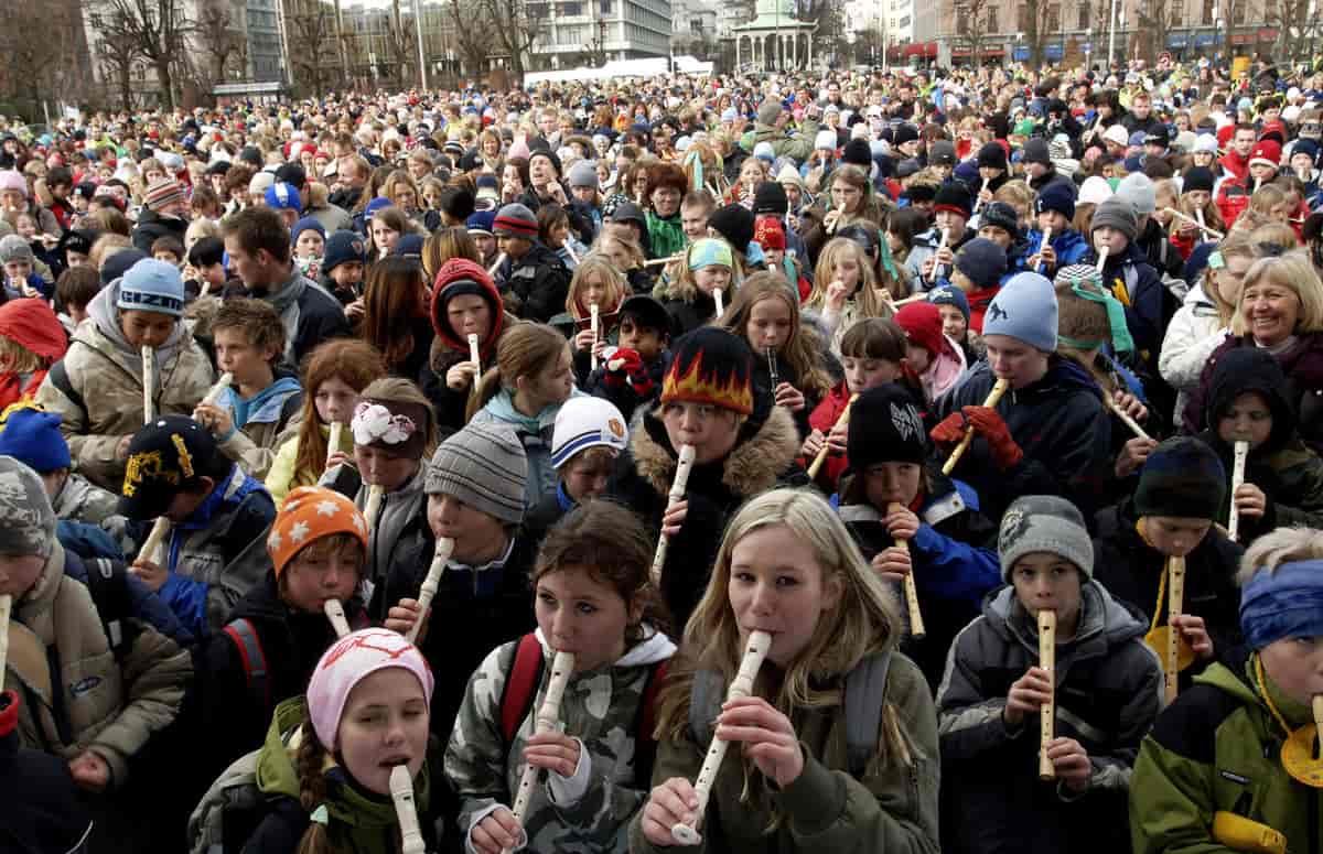Mange skolebarn som spiller på blokkfløyte samtidig ute på en plass.