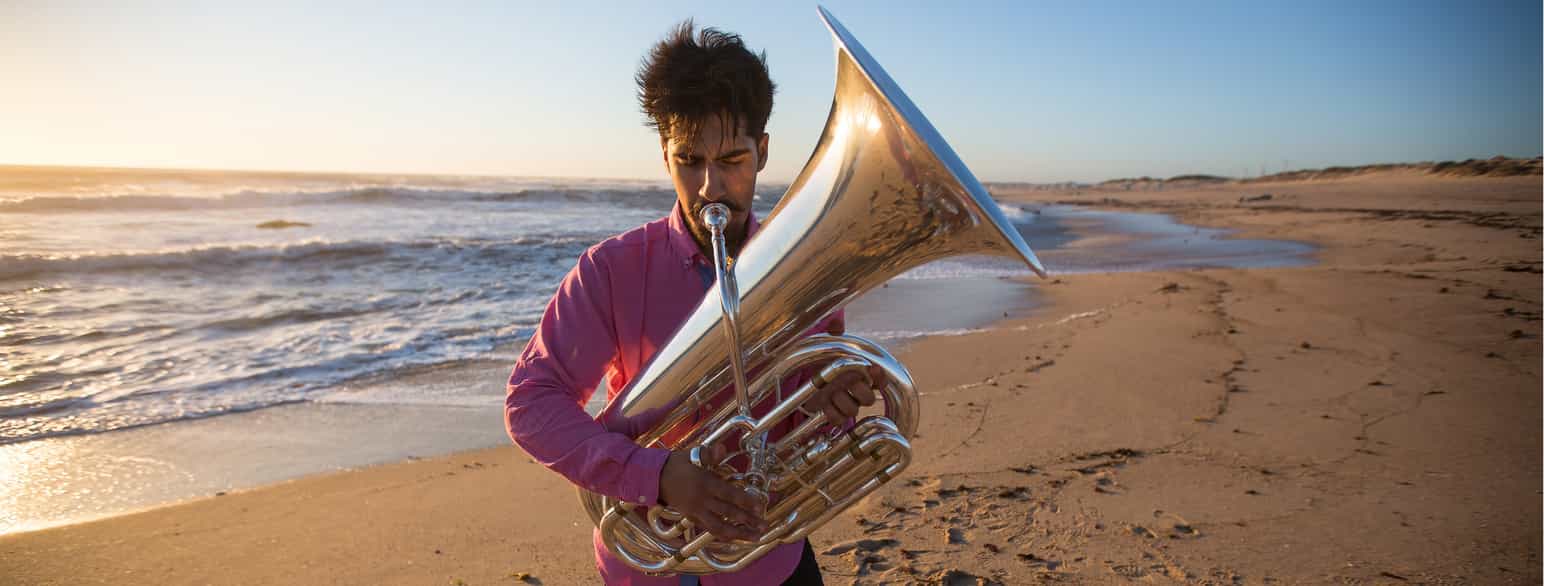 Nærbilde av en mann som spiller tuba på en strand.