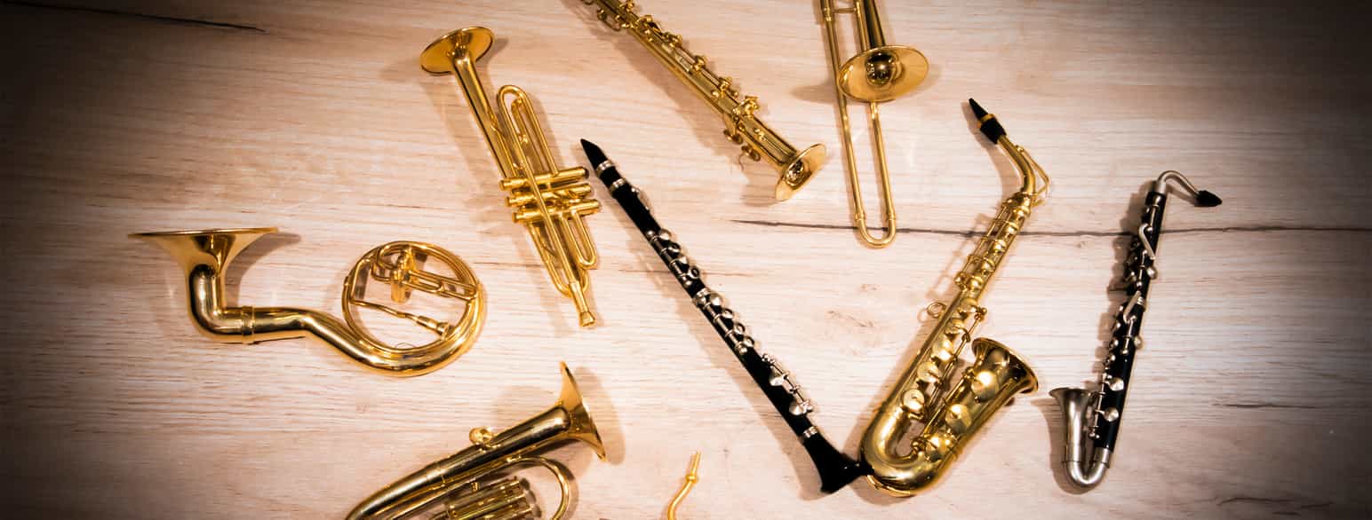 Forskjellige blåseinstrumenter som ligger på et gulv. man ser klarinett, trombone, kornett, saksofon