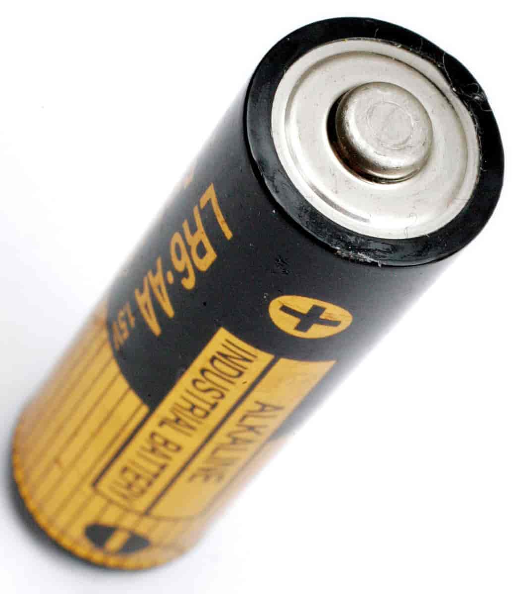 Nærbilde av et avlangt, rundt batteri i svart og gult. Det står Alkaline og AA på batteriet.