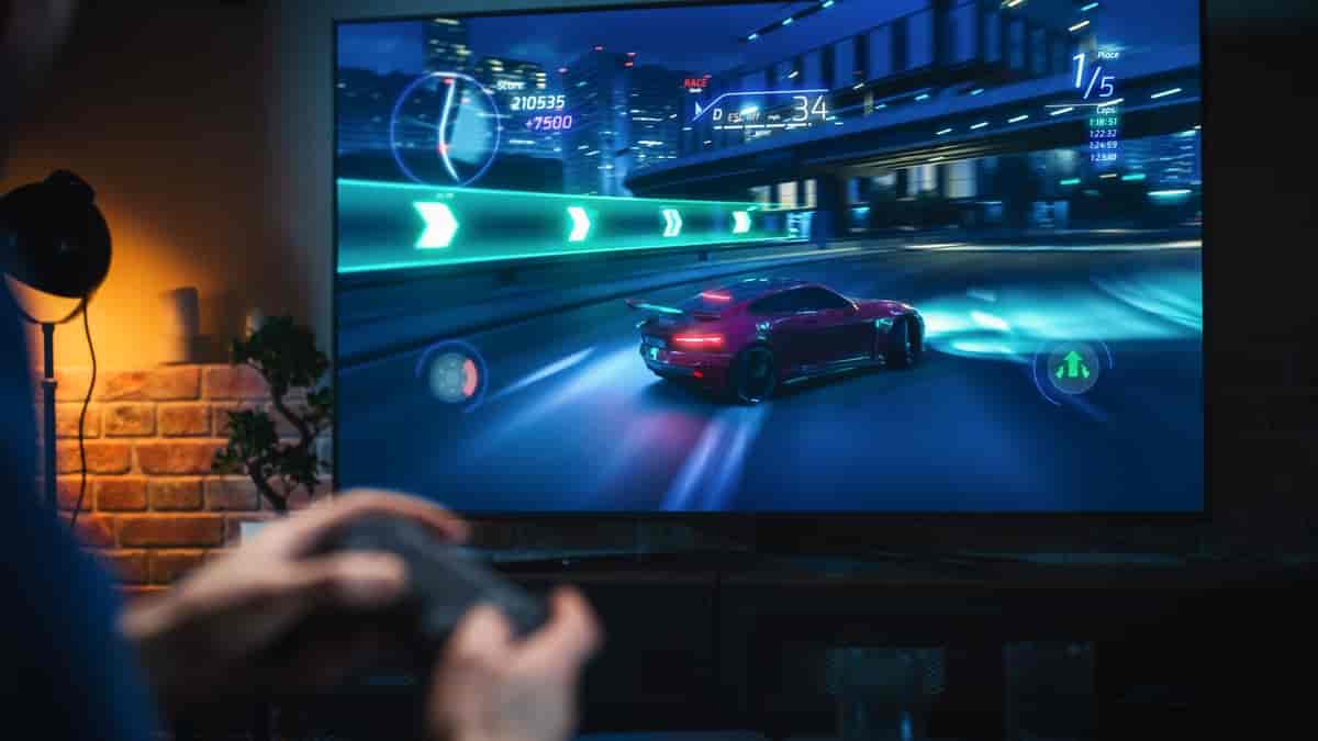 Bakhodet på en som sitter foran en dataskjerm. På skjermen ser man et bilspill, med en svart bil i sentrum.