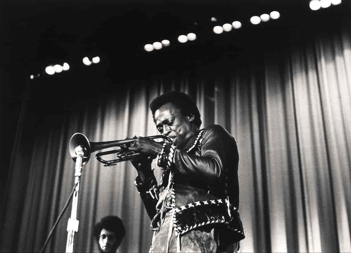 Svart/hvitt bilde av en svart mann som spiller på trompet inn i en mikrofon.