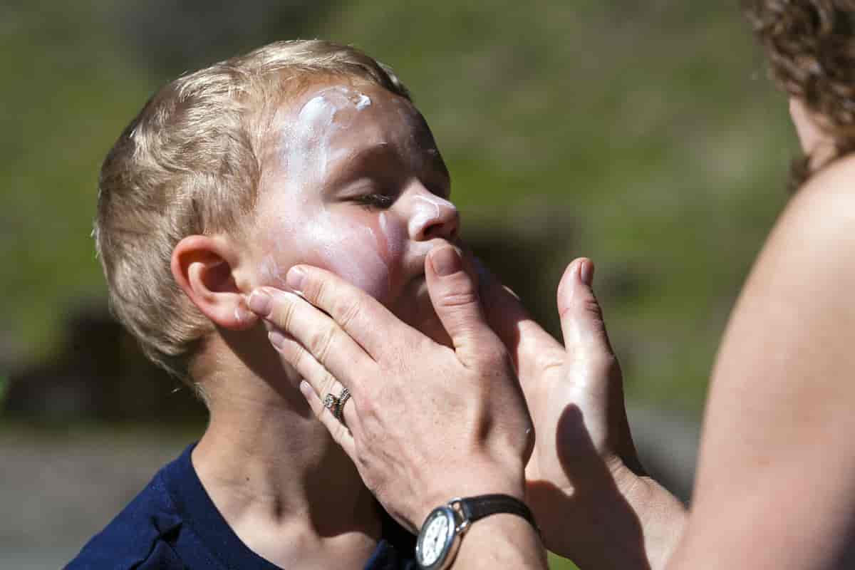 Et barn som får ansiktet smurt inn i solkrem av en voksen kvinne.