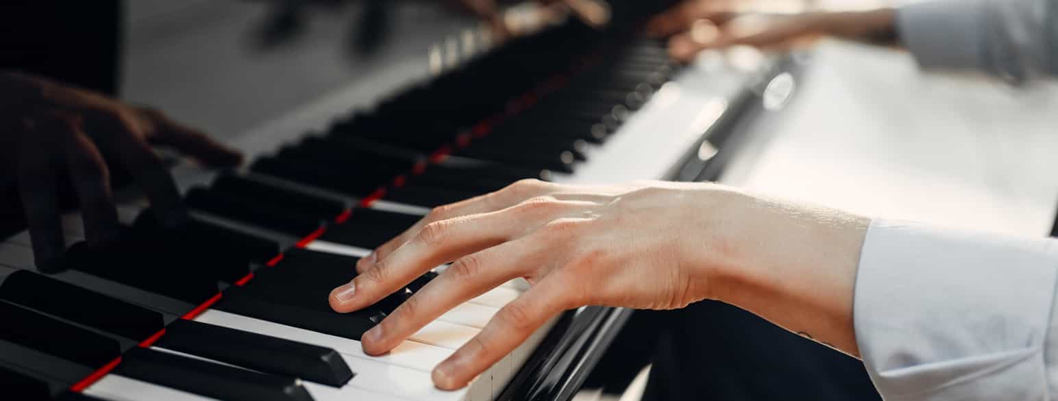Nærbilde av en hånd som ligger på svarte og hvite tangenter på et piano.