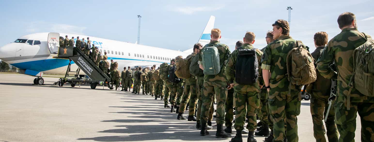 En lang kø med soldater i grønn-brun kamuflasje-uniform på vei inn i et fly. Foto
