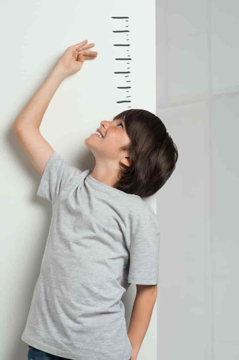 Et barn får målt høyden sin. Barnet står foran en vegg der det er tegnet streker for å vise hvor høy man er.
