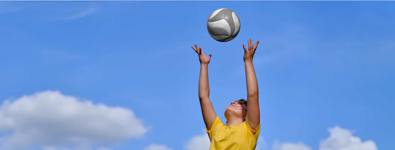 En kvinne som kaster en ball opp i luften mot en blå himmel.