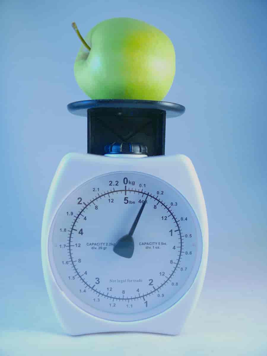 En hvit kjøkkenvekt med et grønt eple på toppen. Vekten viser 0,6 kilo.