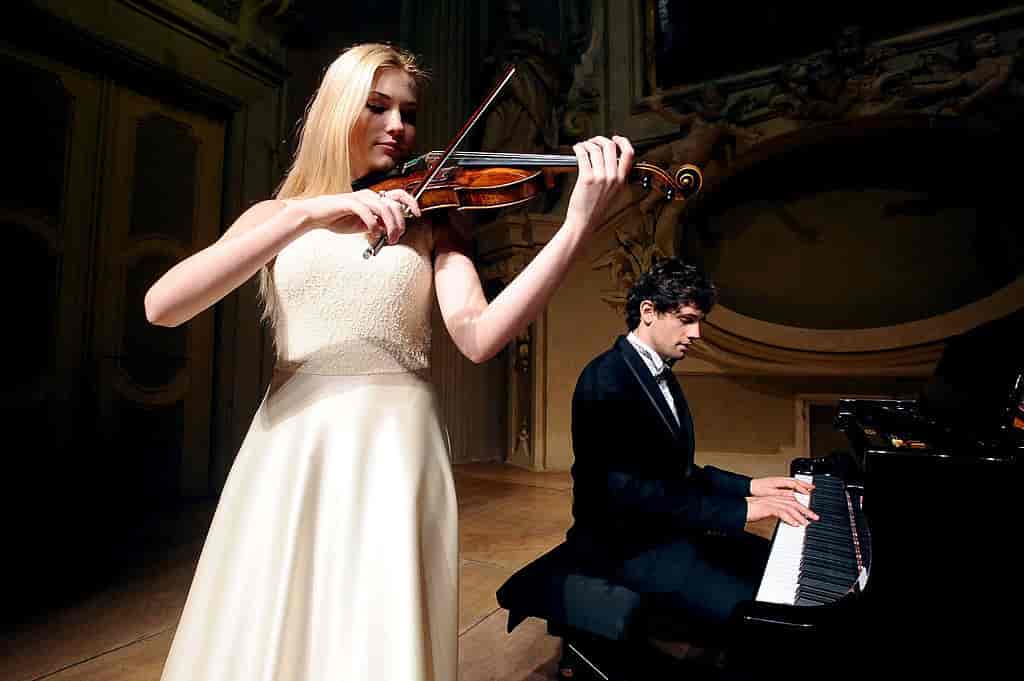 I forgrunnen spiller en kvinnelig fiolinist. Bak kan man se en mann som spiller piano.