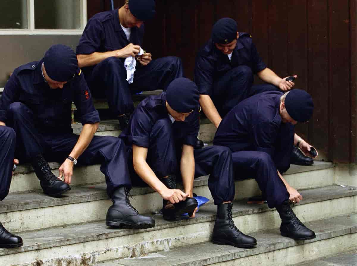 Soldater i mørkeblå uniformer og bereter pusser militærstøvlene sine på en steintrapp.
