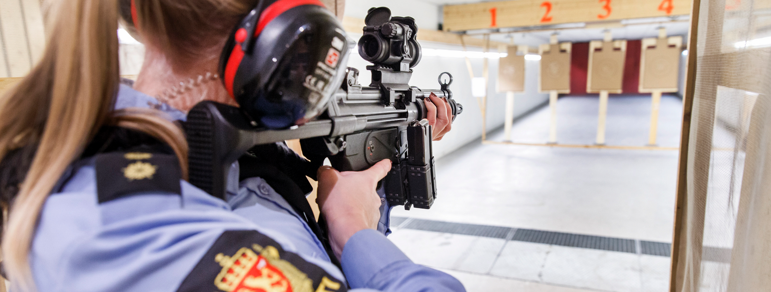 Innendørs skytebane. Nærbilde av en person med automatgevær som sikter mot en blink. Foto