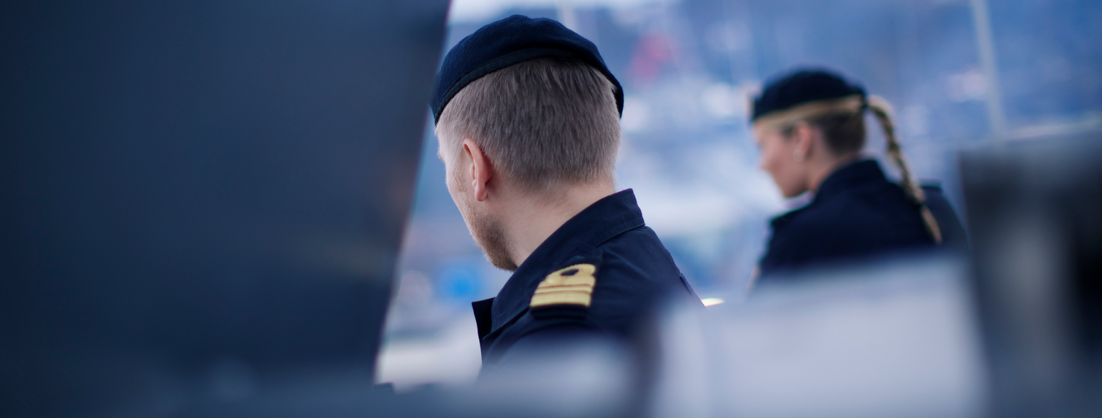 Nærbilde av bakhodet og skulderen til en person i mørk blå uniform og beret. På skulderen har han et merke med en gul løkke over to gule striper. Foto