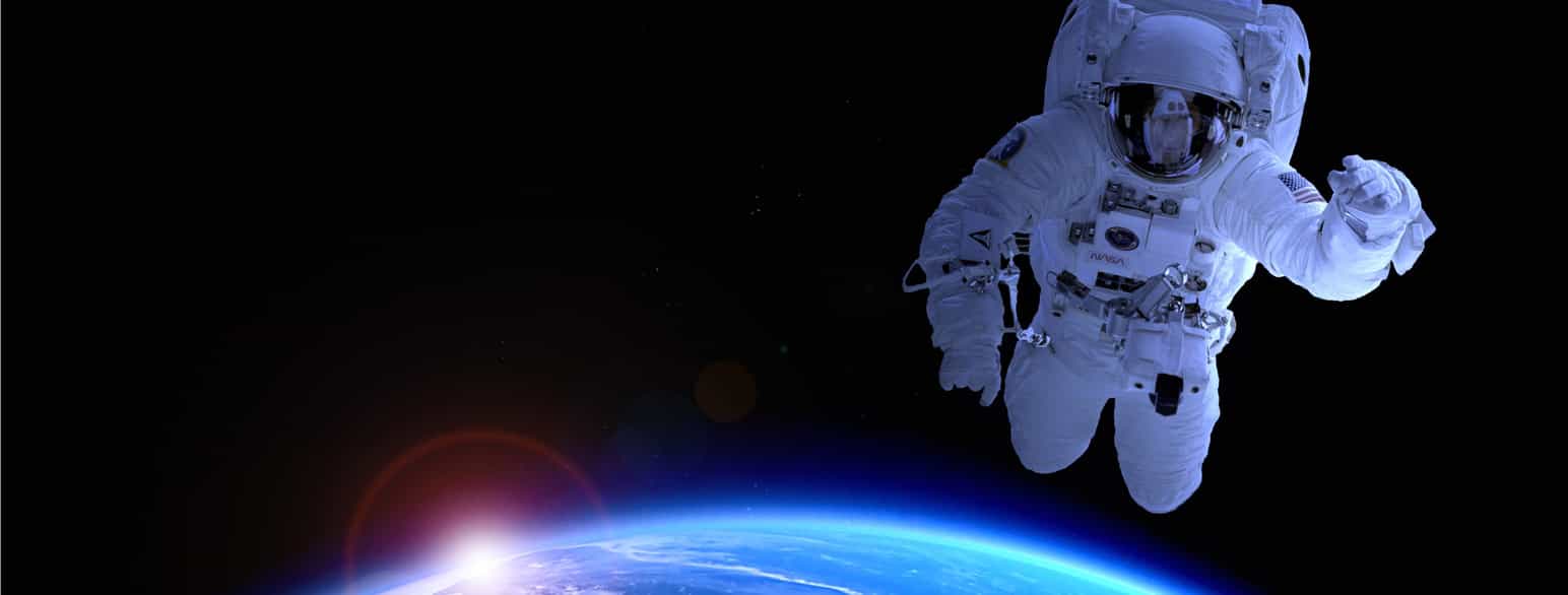 En astronaut ute i verdensrommet. Til venstre skimter man litt av jorda og i bakgrunnen er det mørke verdensrommet.