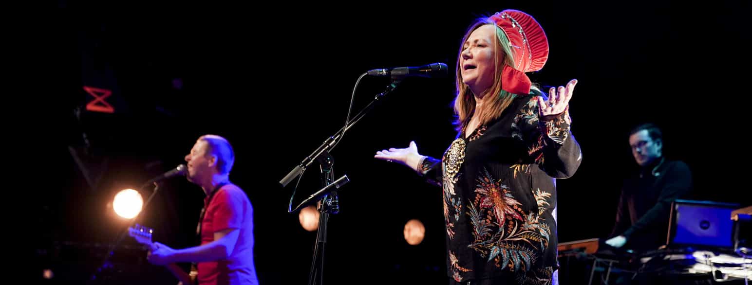 En kvinne synger inn i mikrofon på en scene. Til venstre for henne står en gitarist som synger inn i en mikrofon.