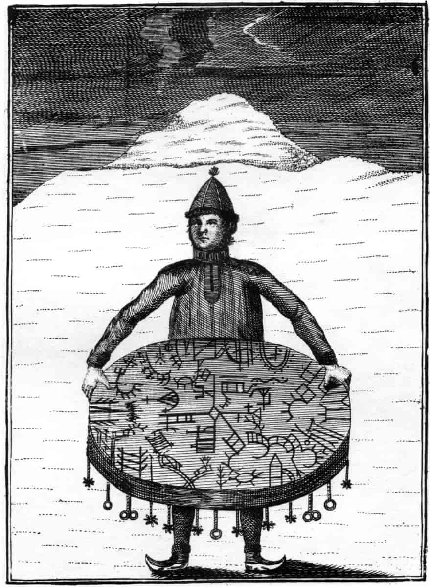Gammel illustrasjon av en person som holder en sjamantromme. Personen har samisk kofte, komager og en spiss lue. Kobberstikk fra 1700-tallet