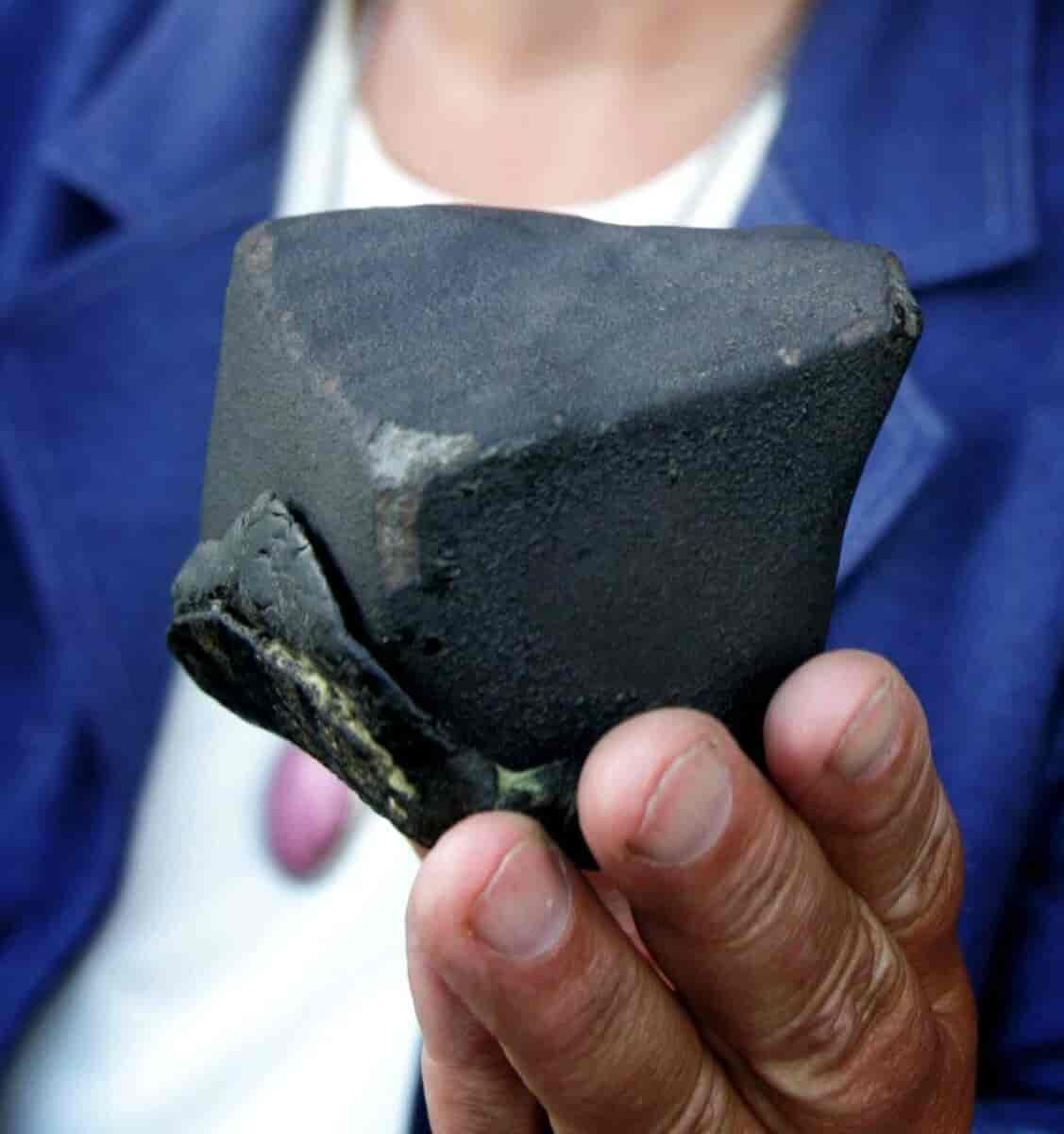 En hånd som holder en svart stein som nesten er formet som en firkant.