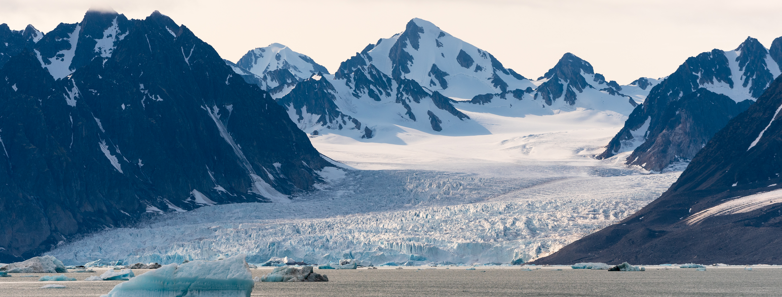 Isbre som ligger mellom spisse bratte fjell. Isen strekker seg helt ned til sjøen i forgrunnen. Foto