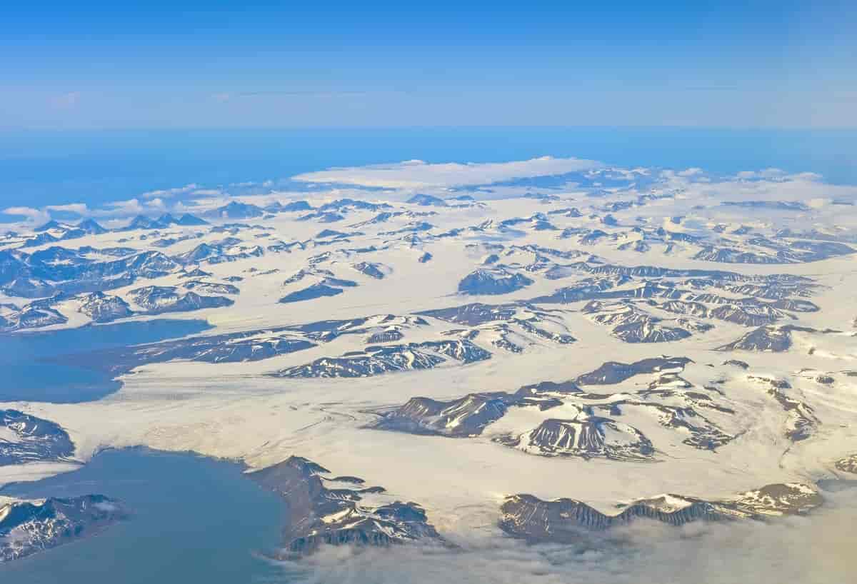Luftfoto av landskap på en øy med spisse fjelltopper dekket av snø og is. Foto
