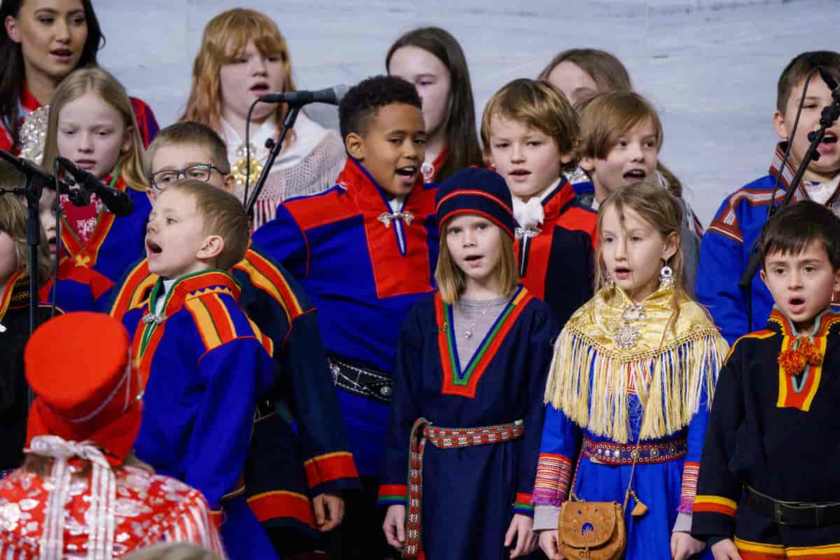 Et barnekor med omtrent 15 barn kledd i forskjellige samiske kofter. Foto